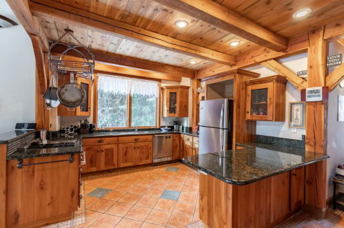 Cozy kitchen with wooden beams, granite countertops, stainless steel appliances, and large windows overlooking nature.